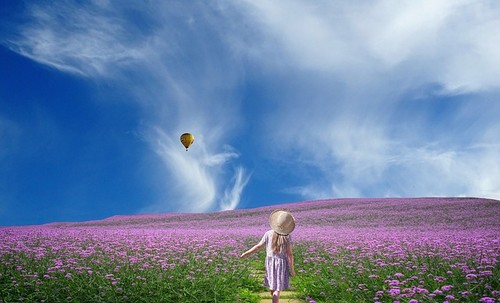 menina de costas num campo florido indo para um balão que desce do céu azul